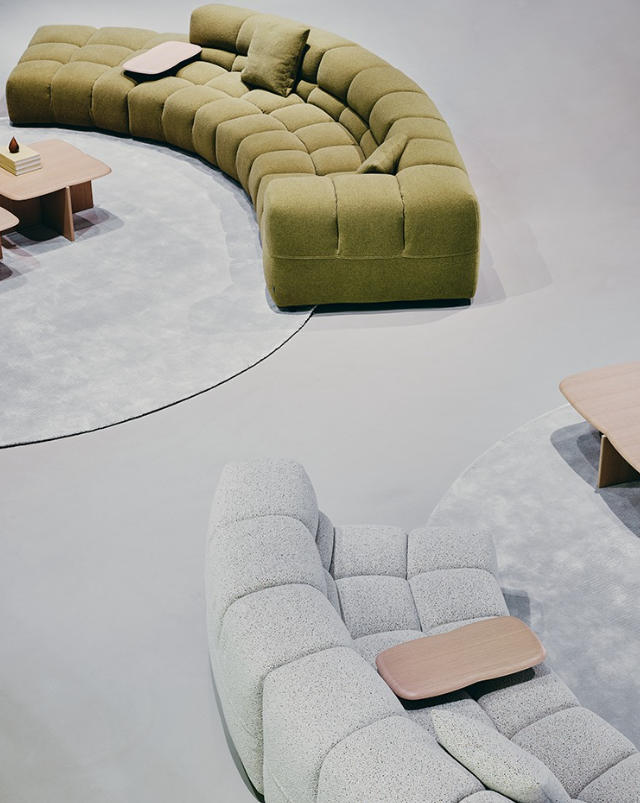 Two curved modern sofas in green and gray with wooden tables on a light gray floor.