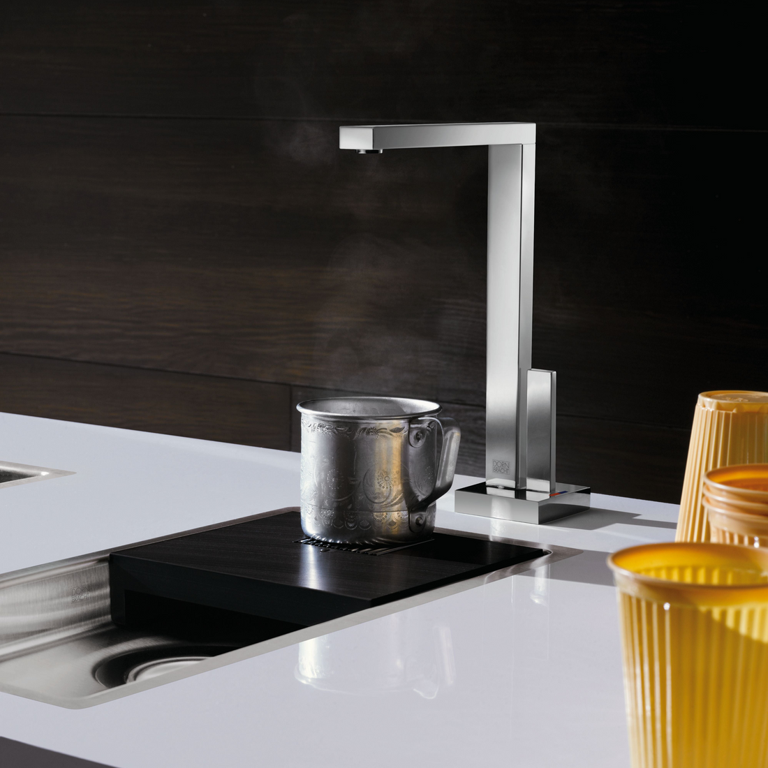 Modern kitchen setup with a faucet, mug on a stove, and yellow cups.
